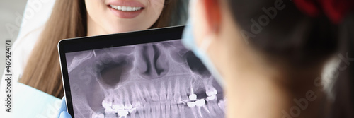 Dentist doctor examines X-ray picture on tablet screen in chair is woman patient