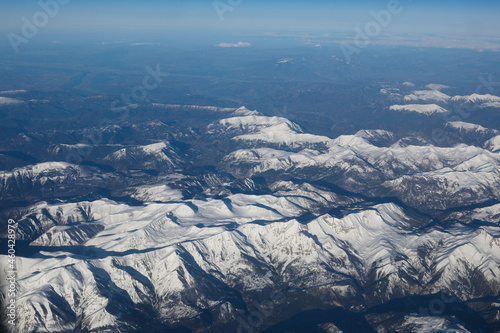 Grenoble France March 23, 2018 View from the airplane window on the snow-capped French Alps mountains. Clear day, light clouds in the mountain valleys.