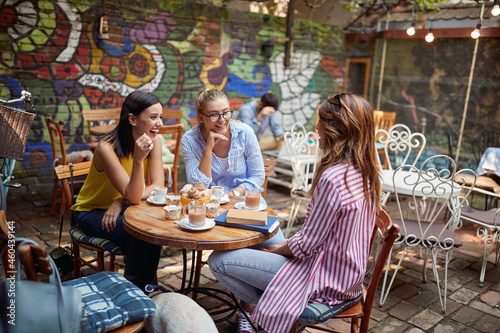 group of three women talking in outdoor cafe, smiling, having a good time