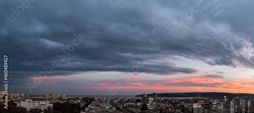 Stormy gray clouds is coming to seaside city at sunset. Panorama of dramatic overcast sky at evening. Dark stratus clouds hang over Varna. Weather change concept. Storm is coming wide landscape. 