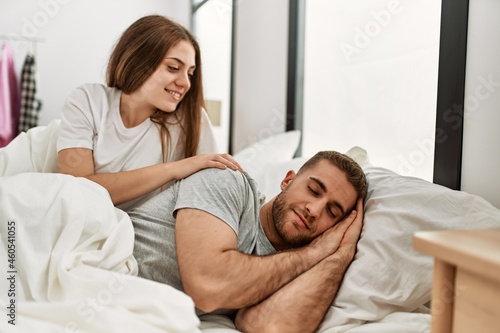 Young caucasian woman looking her sleepy boyfriend at bed.