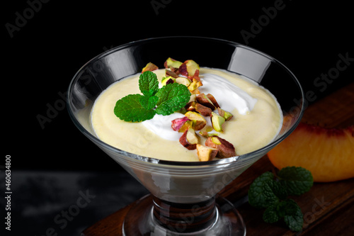 Mango dessert with yogurt topped with pistachio and mint in glass bowl against the black background. Exquisite dessert