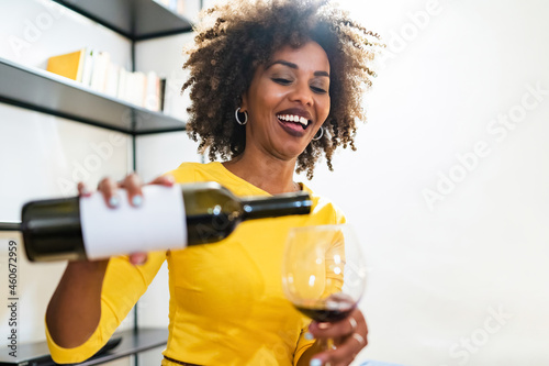 A smiling African woman pours wine into her goblet.