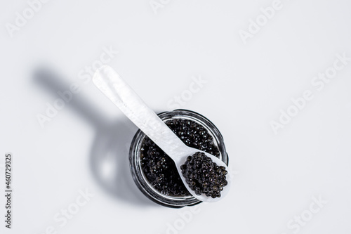 A mother-of-pearl spoon of black caviar resting on small jar