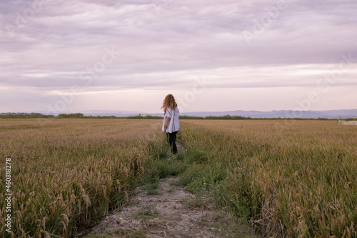 Woman in a shirt walking through a rice paddy at sunset