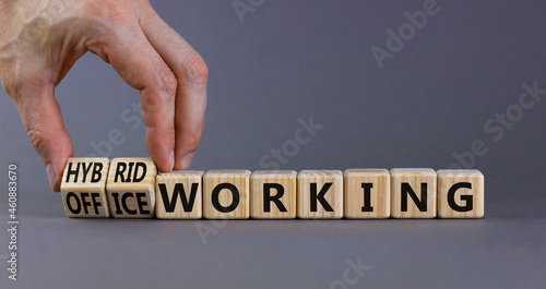 Hybrid or office working symbol. Businessman turns cubes and changes words 'office working' to 'hybrid working'. Beautiful grey background. Business, hybrid or office working concept, copy space.