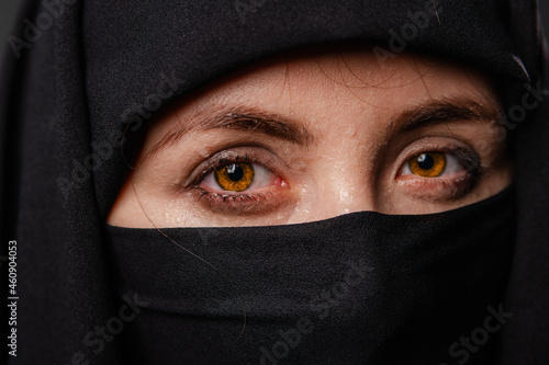 Close up portrait of young, adult woman in black burqa with hidden face, isolated on black background.