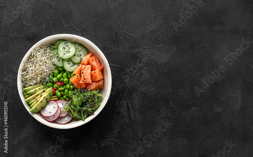 Keto diet poke bowl with salmon, avocado, and edamame beans. over dark background. Banner, top view, copy space.