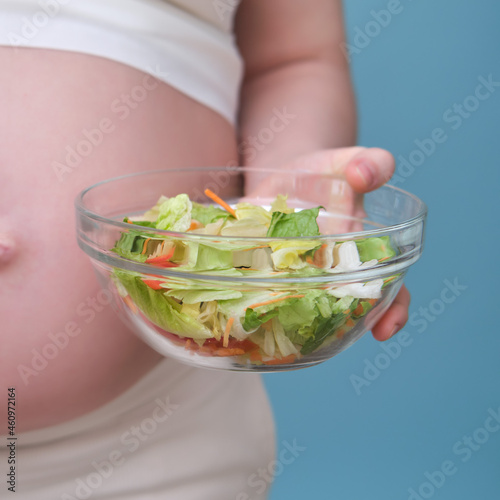 Pregnant woman with a bowl of salad, studio shot on a blue background