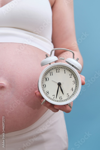 Pregnant woman with an alarm clock in her hands, blue background