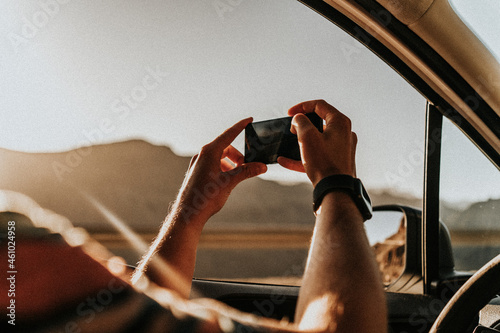 A man is holding a phone while taking photos during the sunset