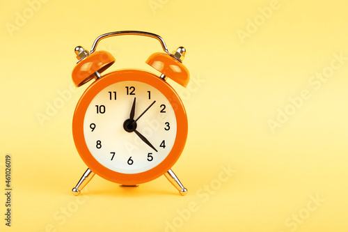Close up one orange alarm clock over yellow background