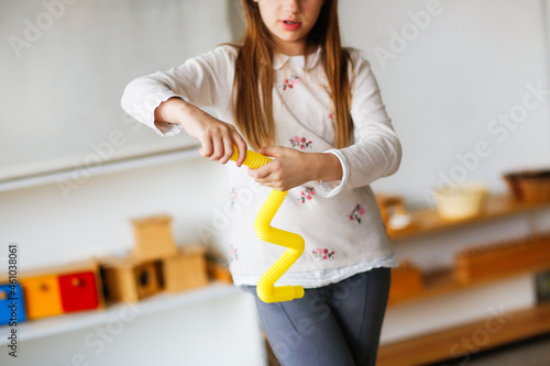 Cute caucasian kid with long hair playing with yellow pop tube, trumpet fashion fidget finger toys, Mini tubes stretch pull tube, in light real interior