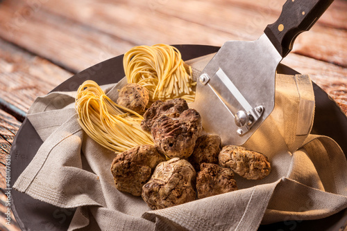 Alba white truffles in napkin with raw egg tagliolini and steel truffle cutter on wooden background