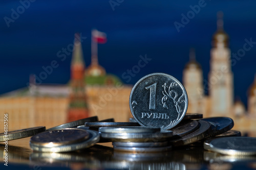 Coin in denomination of 1 Russian ruble on a pile of other coins in front of symbolic out-of-focus fragments of the Moscow Kremlin