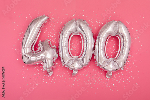 From above of silver shiny balloons demonstrating number 400 four hundred pink background with scattered glitter