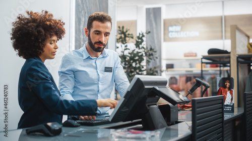 Clothing Store Checkout Cashier Counter: Female Retail Sales Manager Explaining to New Male Assistant Employee Everything He Needs to Know About Working at Fashionable Shop with Stylish Brand Designs.