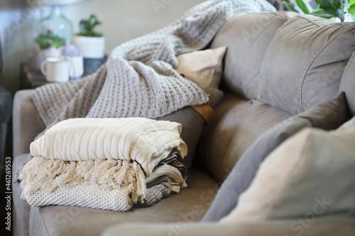 Stack of a variety of soft knit throw blankets stacked on a grey couch in a farmhouse style living room. Selective focus on covers with blurred foreground and background.