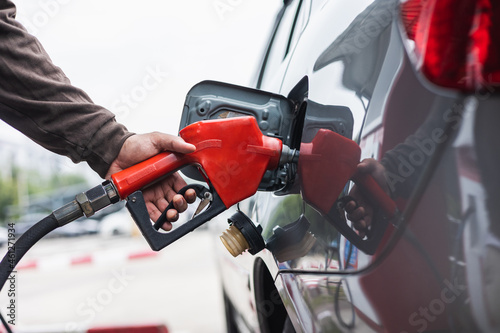 A gas station worker holds a fuel dispenser to fill the car with fuel. A young man's hand holds a gas nozzle to refuel with self-service in a gas station.