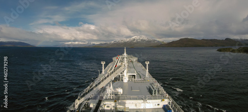 The gas carrier passes through the Strait of Magellan with a rainbow, clouds and mountainous landscape on the horizon.