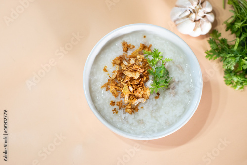 Rice gruel or soft-boil rice with pickled garlic and parsley in white bowl on warm background.
