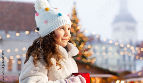 winter holidays and children concept - happy little girl with cup of hot tea over christmas market at old town hall square, tallinn, estonia