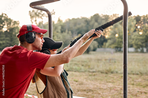 Nice caucasian man in headset is confidently teaching female to use rifle, weapon on outdoor range, Handsome male and pleasant lady in protective clothes equipment outfit learning to shoot