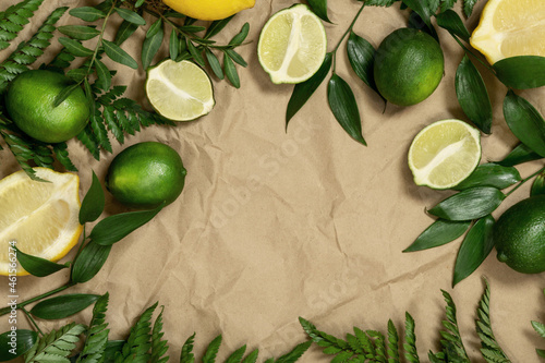 Creative background of tropical fruits with leaves, lemon, lime, on a with fresh branches of fern and greenery on craft paper. Creative craft paper background.