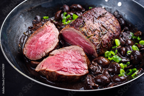 Traditional fried dry aged angus beef filet roast and medaillon natural with mushrooms in red wine sauce served as close-up in classic skillet
