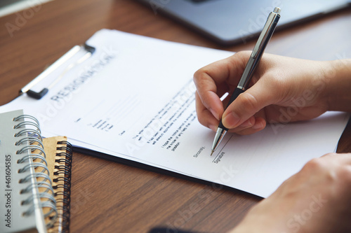 Close up businesswoman hand signing her resignation letter on his desk before sending it to his boss to quit a job. unemployment and change job concept