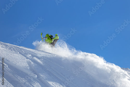 snowmobiler. prof is a snowmobile pilot in a bright jumpsuit and helmet, riding uphill at high speed with swirls of snow. the concept of advertising outdoor activities and travel in winter