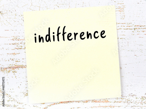 Yellow sticky note on wooden wall with handwritten word indifference