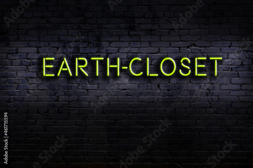 Neon sign. Word earth-closet against brick wall. Night view