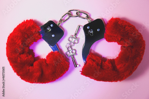 Red sexy fluffy handcuffs with keys on a pink background.