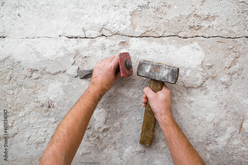 Young adult man hands using sledgehammer, metal stone chisel and removing old concrete on floor. Closeup. Point of view shot. Preparing for repair work of home. Flooring restoration. Top down view.