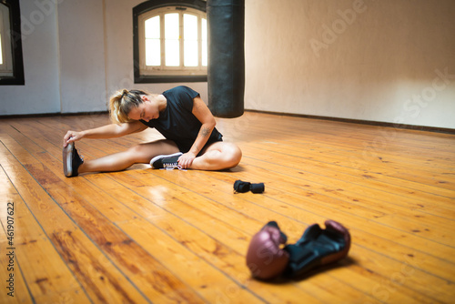 Young woman stretching for training. Attractive woman in black sport clothes sitting on floor, training. Sport, healthy lifestyle, boxing concept