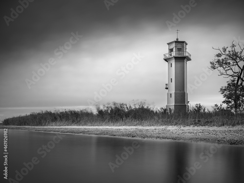 calm water and view to lighthouse under dark sky in photo of vintage style