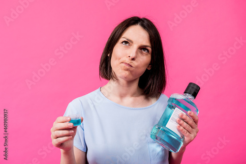Beautiful girl uses mouthwash on the pink background