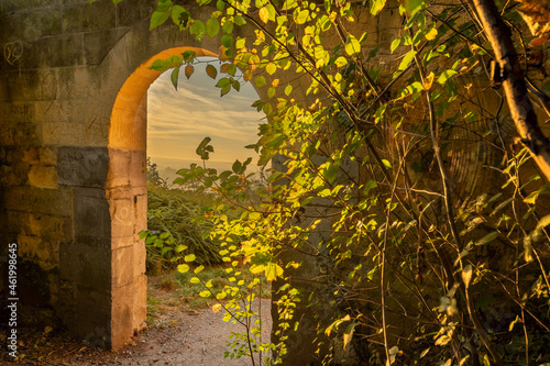 A look through a marl stone gate with a view on the vineyards and a golden colored sunrise on a misty morning in October on the hills just outside Maastricht.