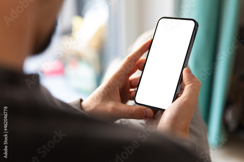 Man using smartphone blank screen frameless modern design while sitting on the chair in home interior