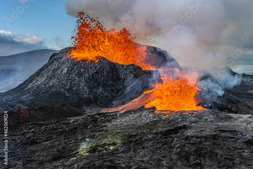 Daytime volcanic eruption on Reykjanes peninsula. Lava shoots up from the crater above. Crater from Fagradalsfjall volcano in Iceland in GeoPark. Clouds and steam in the sky