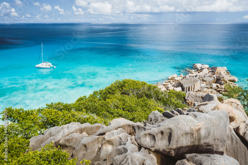 Aerial of Grand Anse beach at La Digue island in Seychelles. White sandy beach with blue ocean lagoon and catamaran yacht moored