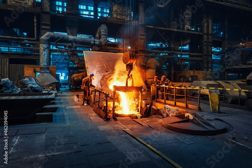 Metal cast process in blast furnace in metallurgical plant or factory. Liquid iron molten metal pouring in container, heavy industry background.