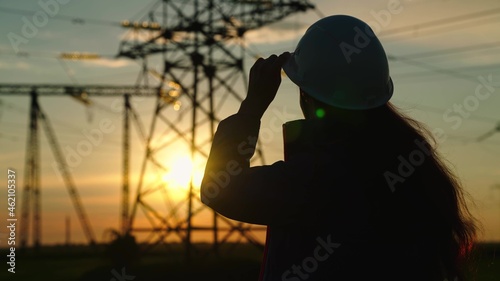 Civil engineer, woman specializing in electricity supply works outdoors. Environmentally friendly electricity. Modern technologies. Power engineer in safety helmet checks power line, digital tablet