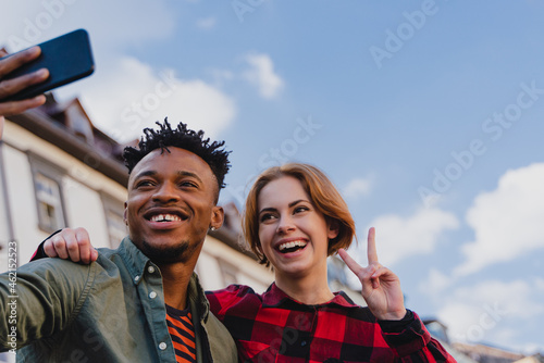 Low angle view of young biracial couple making selfie for soial networks outdoors in town.