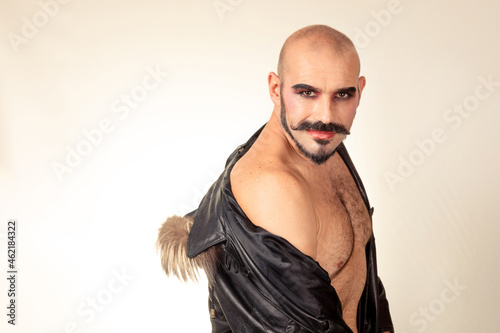 Caucasian man in makeup with bare back and leather jacket looks at camera while smiling. Theme masculinity and inclusion