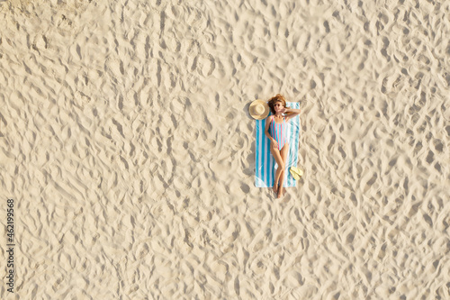 Woman sunbathing on beach towel at sandy coast, aerial view. Space for text