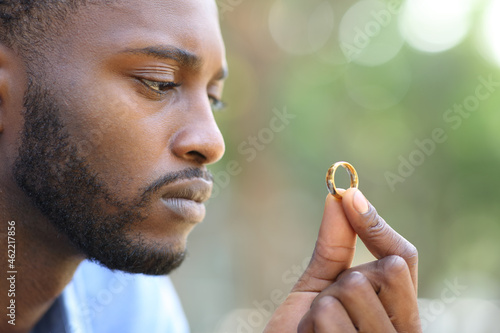Sad black husband doubting holding wedding ring