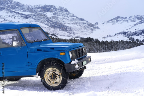 close-up of a blue SUV with iron chains on wheels against the background of the Alpine mountains, the concept of the safety of movement of cars with snow chains on tire on a winter road