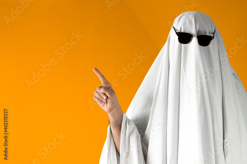 Person in Halloween costume of ghost with sunglasses points away